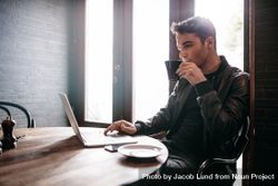 Man sipping coffee in cafe while working on laptop 0vzOR0