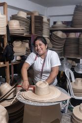 An adult Hispanic woman is smiling while working in a hat workshop