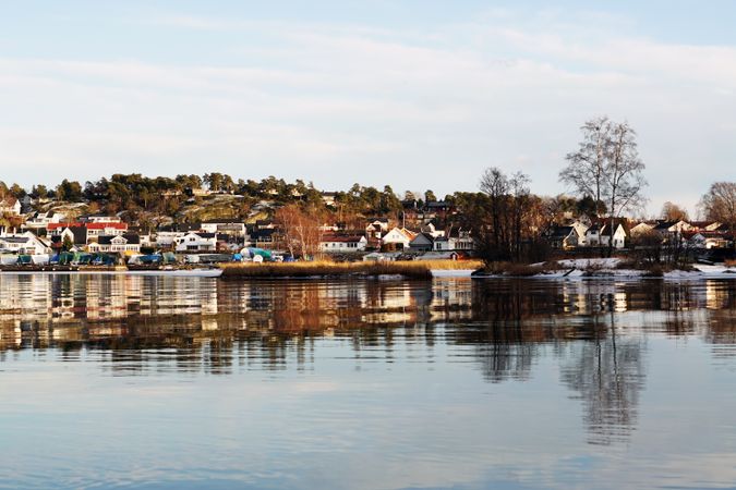 Town at snowy river side and bare trees reflecting in still water