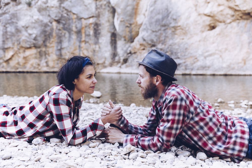 Positive woman and man resting on stone shore near river