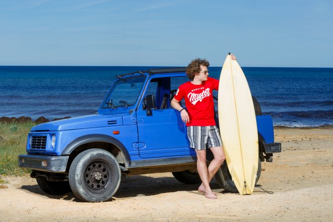 Guy with big surfboard near car on beach