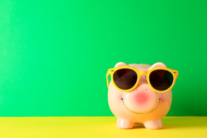 Happy piggy bank with sunglasses on color table against green background, space for text. Finance, saving money