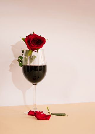 Glass of red wine with rose in it and fallen petals