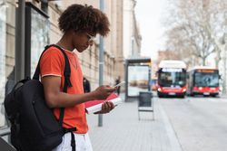 Black male student waiting for bus on street