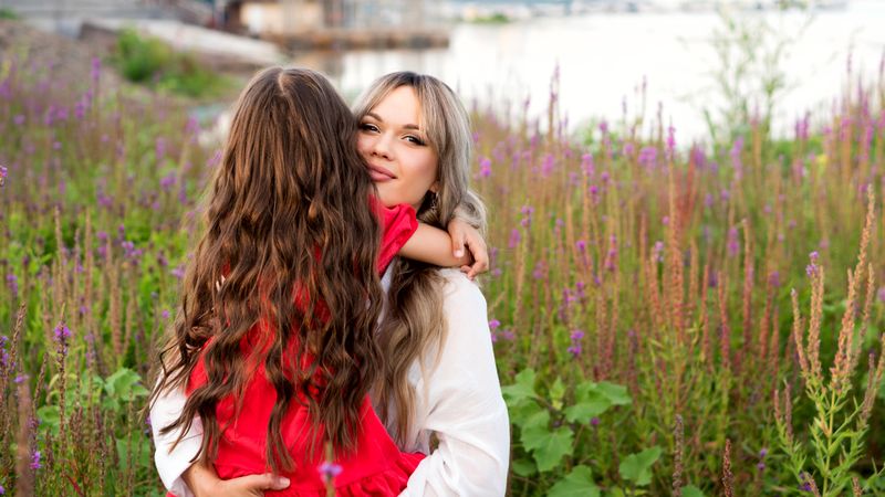 Mom and little daughter walking among meadow flowers