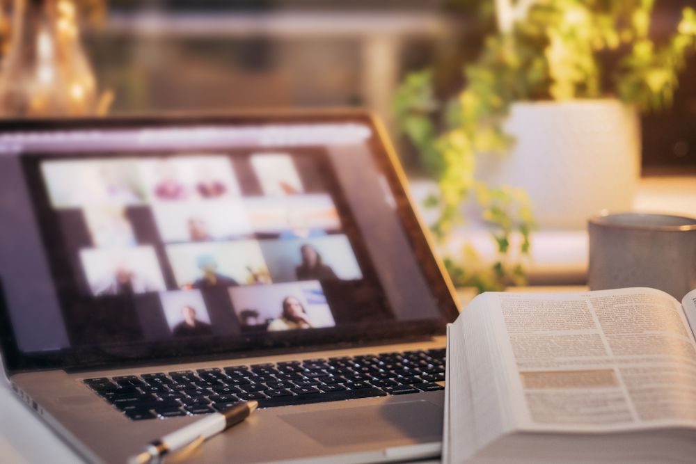 Online video meeting running on a laptop beside an open book
