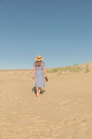 adult woman standing with book on sand dune on hot summer day