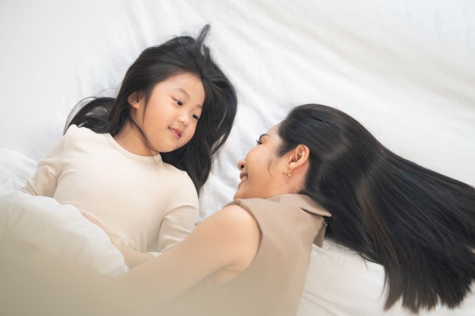 Top view of Asian mother and daughter cuddle and talking on bed.