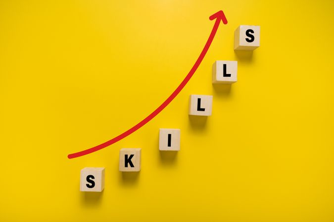 wooden blocks with skills words and red up arrow. isolated on yellow background. concept of upgrade skills