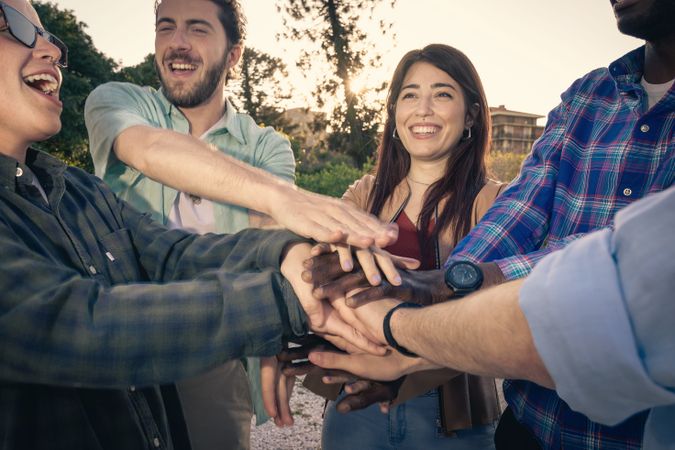 Close-up of a diverse group of happy friends putting their hands together in a huddle.