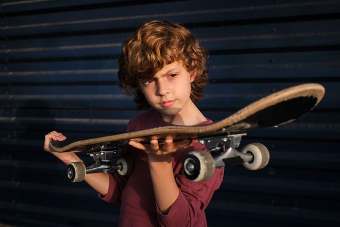 Boy examining skateboard against blue wall