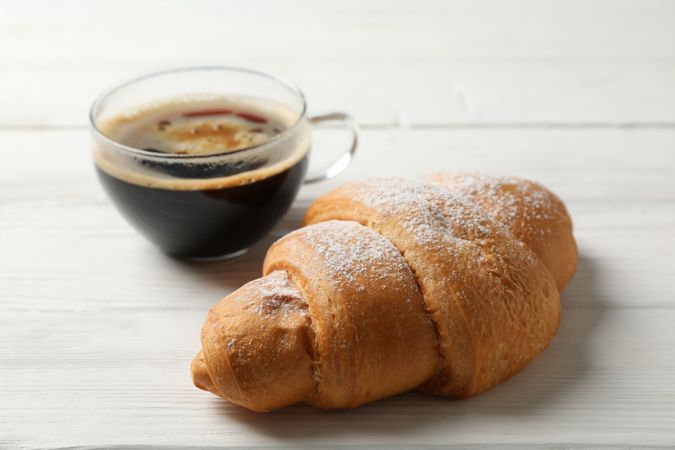 Cup of coffee and croissant on wooden table, close up