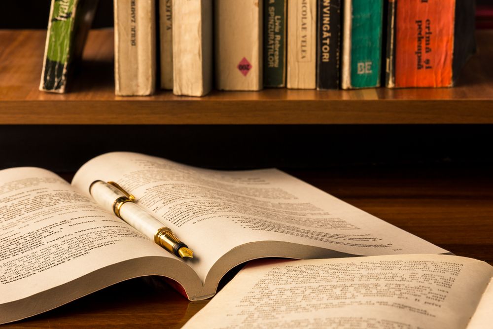 Open book with golden pen near wooden book shelf