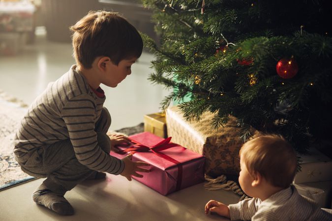 Boys picking up gifts from under the Christmas tree with baby nearby