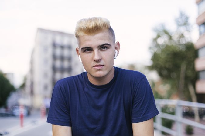 Portrait of serious blond man with earbuds on the street while looking at the camera