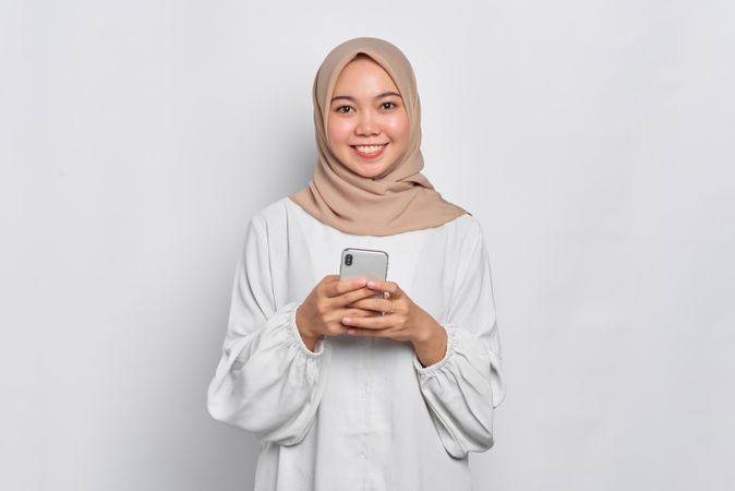 Happy Asian female in headscarf looking up from cell phone