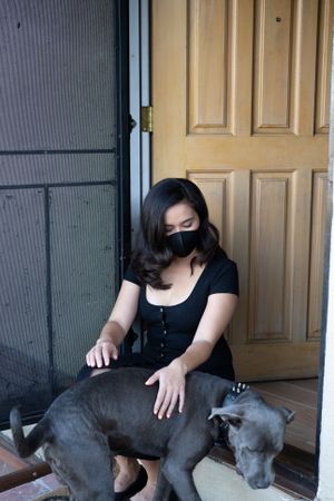 Woman sitting at doorstep with mask on petting her dog