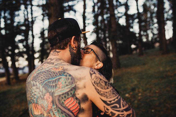 Young guy in tattoos hugging woman in forest