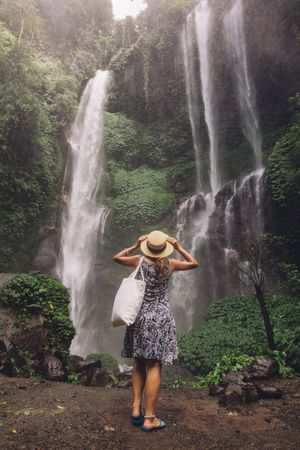 Rear view shot of female tourist admiring beautiful waterfall in tropical rain forest