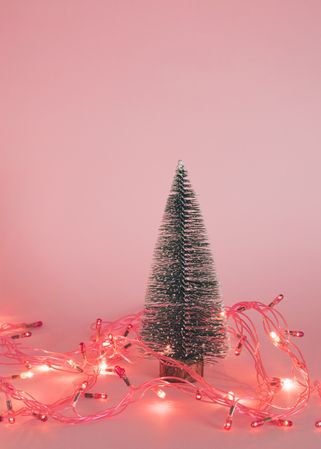Christmas tree surrounded by fairy lights on pink background