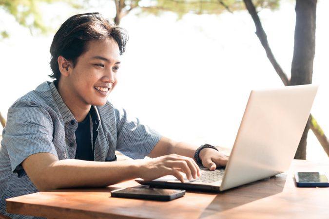 Happy Asian Young businessman work at outdoor with laptop. Concept of remote and freelance work. Young successful man wearing casual blue cloth.