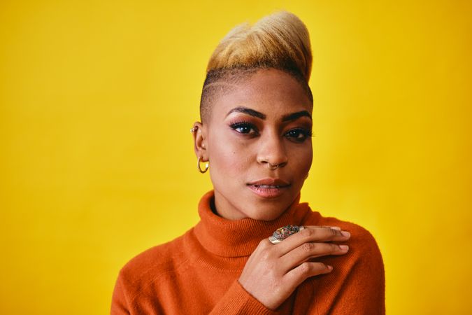 Studio shot of confident Black woman with short blonde hair in orange sweater