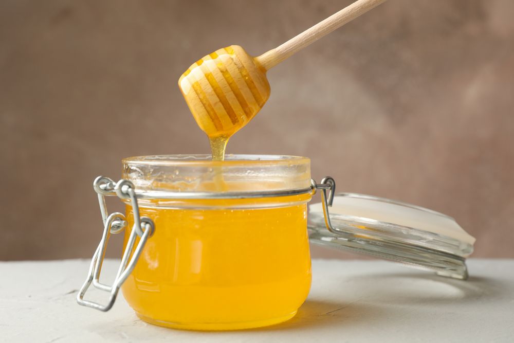 Glass jar with honey and dipper on neutral background, close up