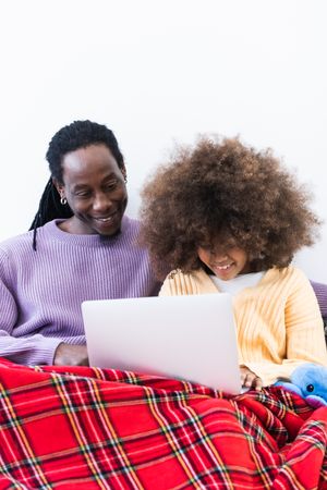 Black father browsing laptop with daughter under plaid