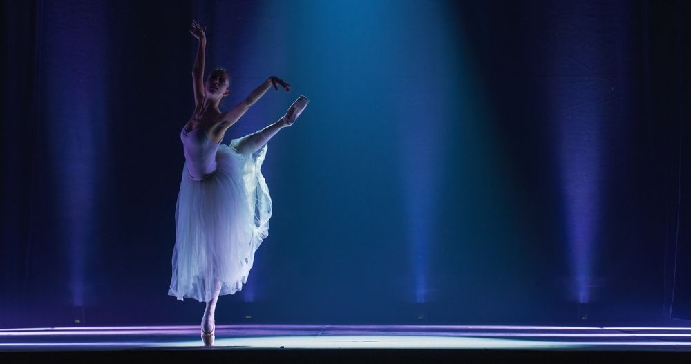 Cinematic Shot of Ballerina in Pointe Shoes and Tutu Dancing and Rehearsing on Classic Theatre Stage with Dramatic Lighting.