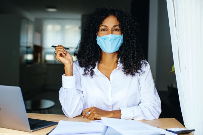 Confident woman holding a pen and working on documents while wearing a facemask