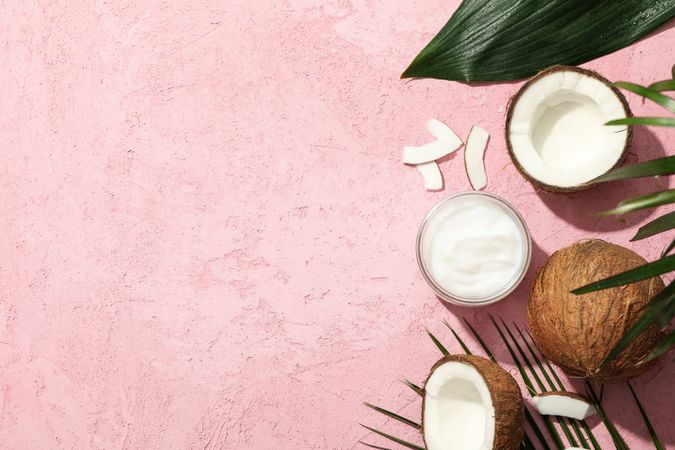 Coconut and cosmetics on pink background, top view