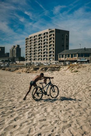 Boy pushing bike on sand in front of building