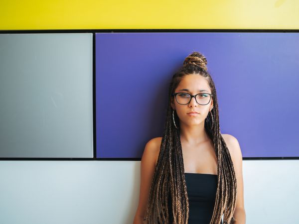 Charming teenage girl with braids in sunglasses nearby colorful wall