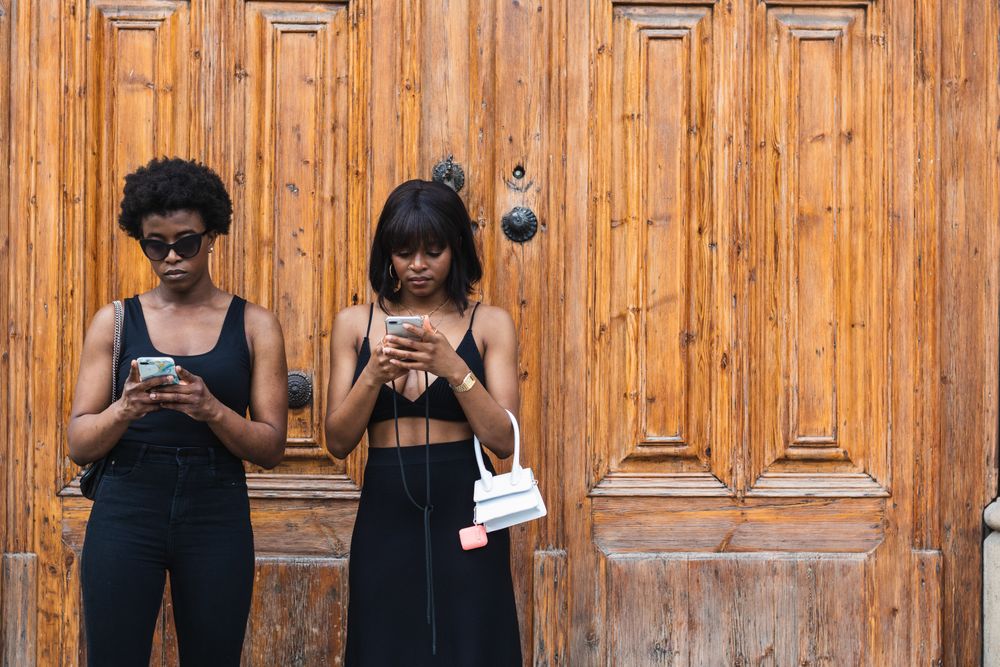 Black females using smartphones while standing on street