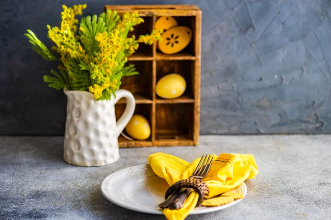Easter table setting on concrete counter with vase of flowers and yellow napkin