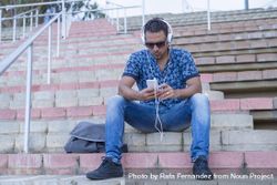 Man in jeans and blue shirt listening to music on smartphone 5Xk7o0