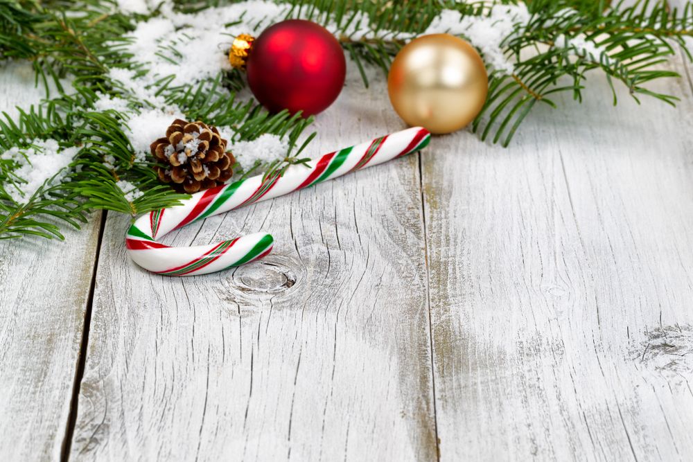 Candy cane with snow covered fir branches and ornaments on rustic wooden boards