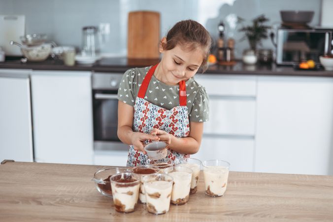 tiramisu making process in the kitchen- little girl making Italian desert with cocoa and espresso-dipped ladyfingers with mascarpone cream