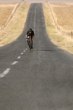 Cyclist riding bike on long asphalt road