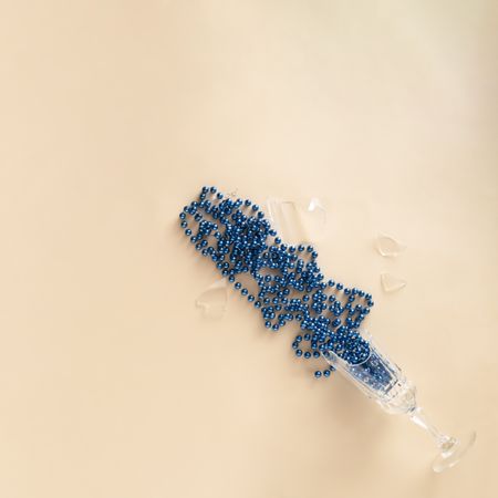 Champagne glass broken on a beige table with blue beads