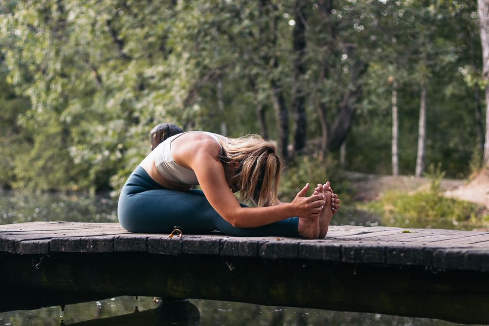 Woman in sportswear doing yoga in nature near a lake
