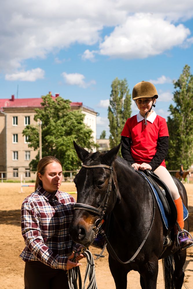 Instructor adjusts young rider's position in equestrian training.
