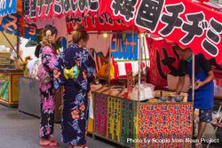 Two women in kimonos standing at a food kiosk in Kyoto, Japan 41OYj0