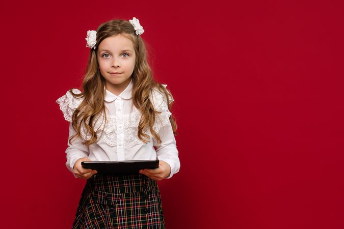 Portrait preteen schoolgirl with tablet PC on vivid red colored background