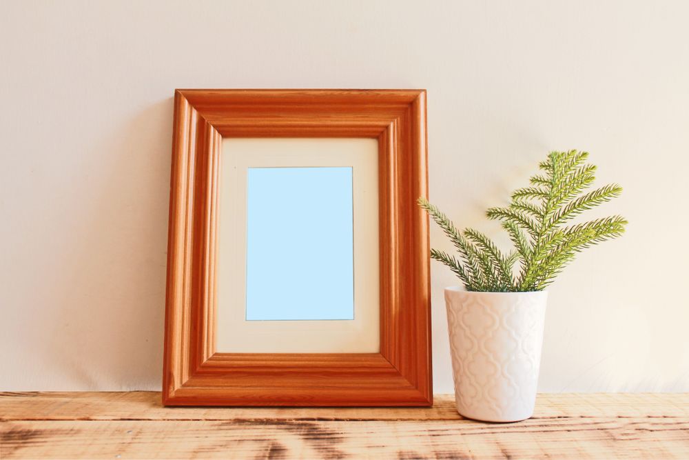 Rectangular wooden picture frame on wooden desk with branch in vase mockup