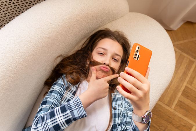 Girl taking playful selfie with hair mustache on smartphone.