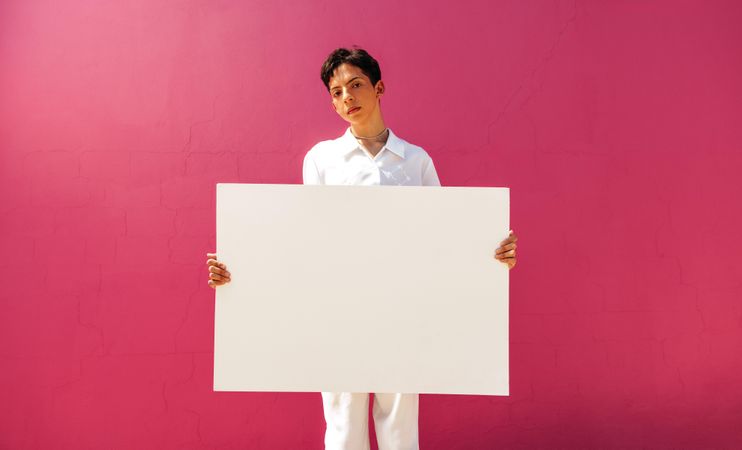 Young male activist displaying a blank poster against pink wall