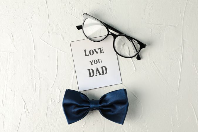 Inscription love you DAD, blue bow tie and glasses on blank background, space for text and top view