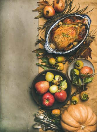 Roast turkey in roasting pan, on table with fall leaves and fruit, vertical composition, copy space