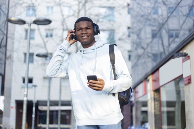 Smiling Black man walking in the street while listening music on headphones